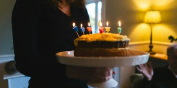 жінка несе святковий торт зі свічками чоловіку