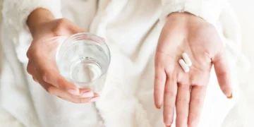 Склянка води поруч із таблетками на столі